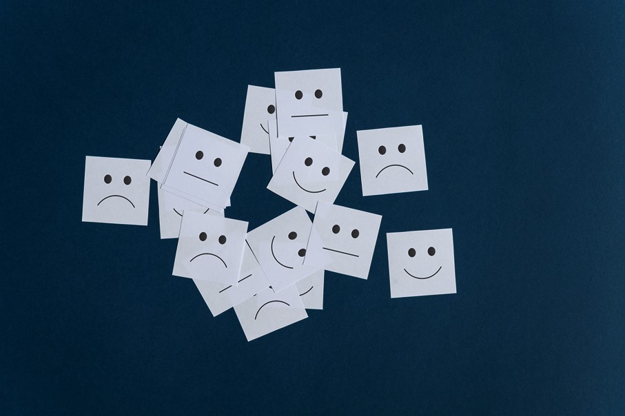 Many white post it papers with smiling sad and neutral faces on them. Over blue background.
